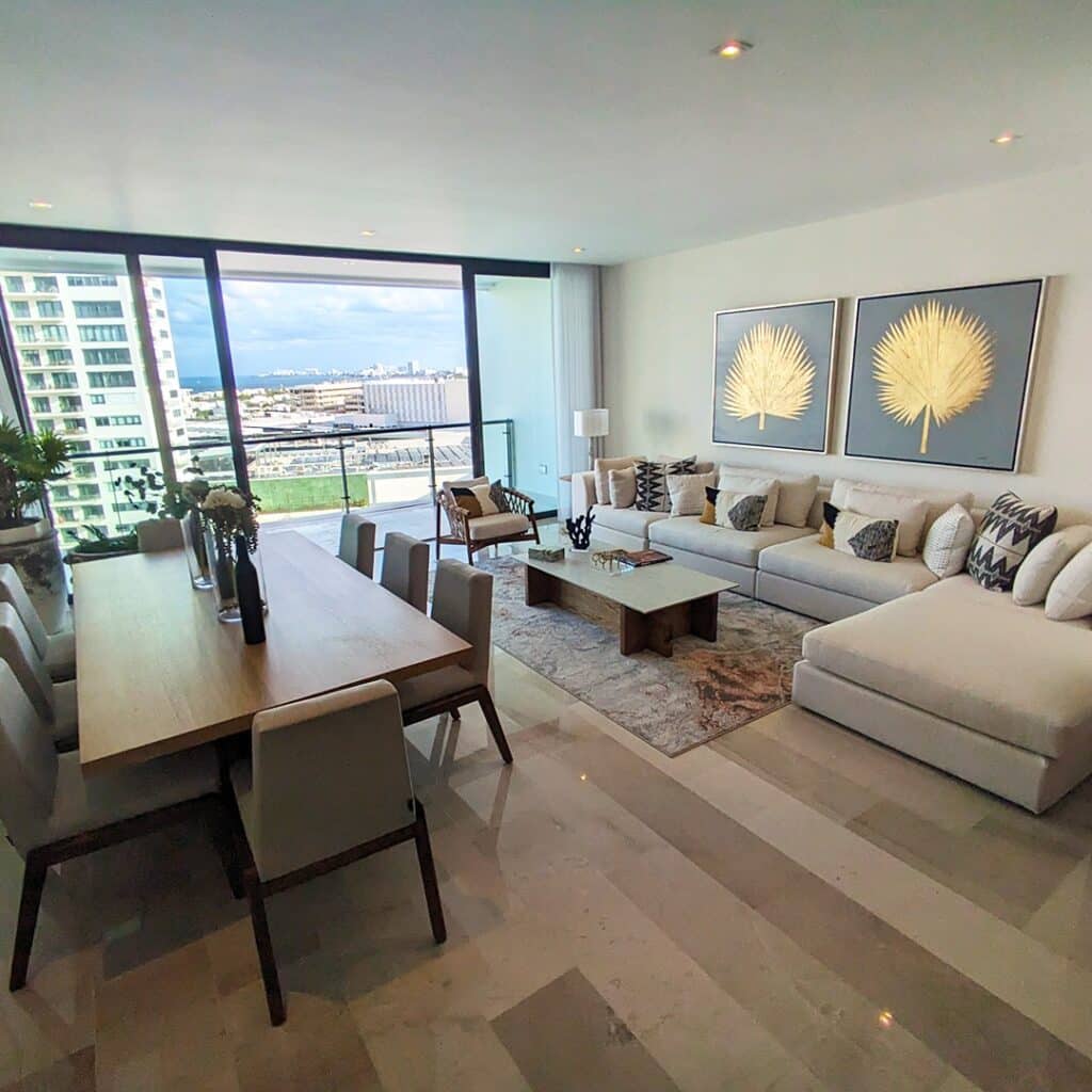 Spacious living area in Blume 1C in Puerto Cancun, featuring a large sofa, modern decor, and a balcony view of the city skyline and coastline.