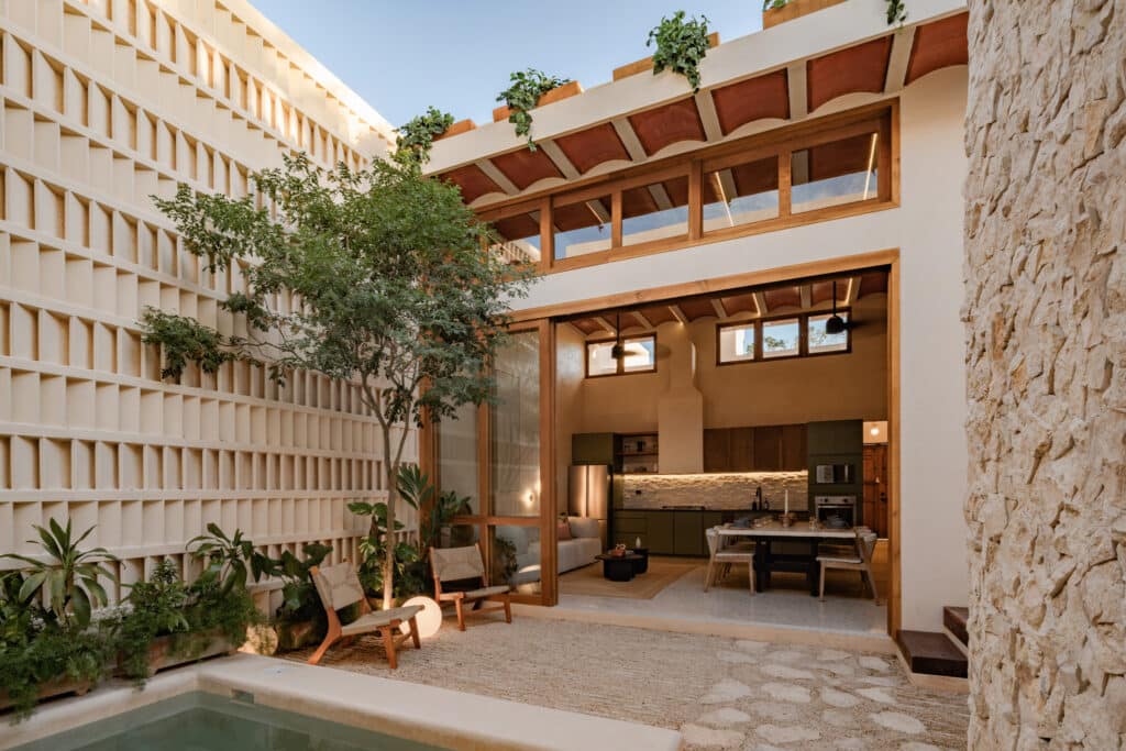 A modern interior view of Casa Caracol Merida Villa 1 in Caracol 525, showing an open living area with wooden accents, large windows, and a cozy outdoor space with a small pool.
