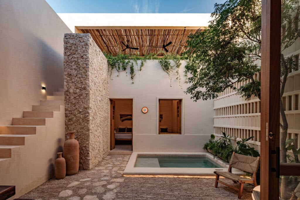 A modern house in Caracol 525, Merida, features an interior courtyard with a small pool, stone accents, lush greenery, and wooden details, creating a peaceful outdoor space.