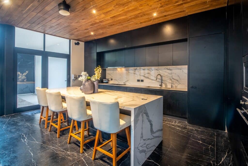 Modern kitchen with black cabinets, a white marble island and backsplash, dark marble floors, and a wooden ceiling in Casa Orion Villa 3, Compostela Orion 61 in Merida.