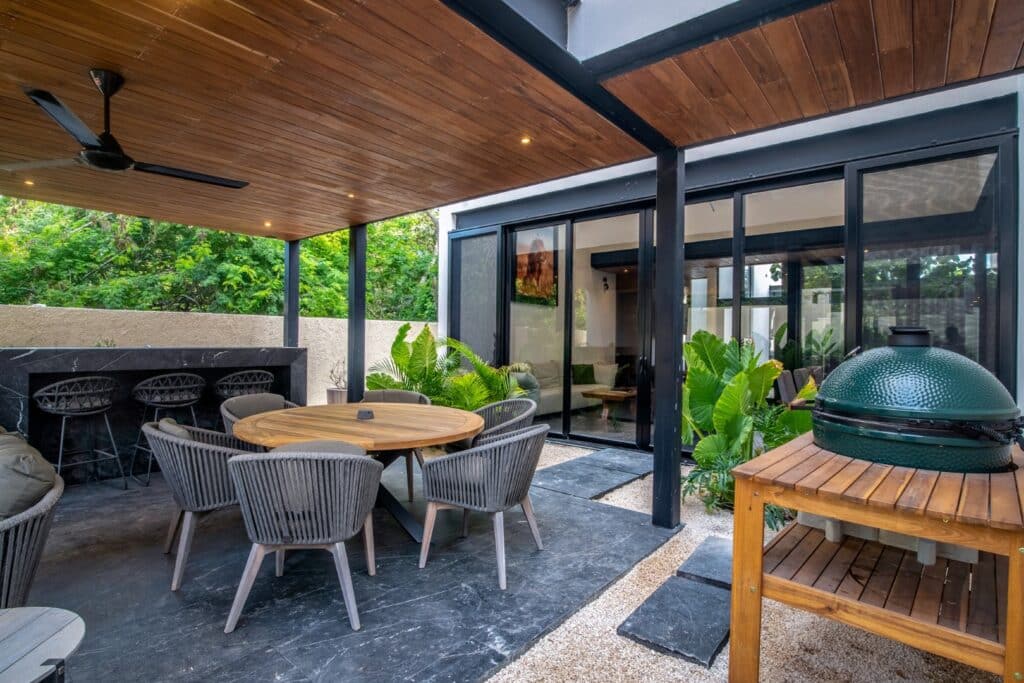 Outdoor patio of Casa Orion Villa 4 at Compostela Orion 61 development in Santa Maria Yaxche, Merida, featuring a wooden ceiling, black-framed glass doors, a round wooden table.