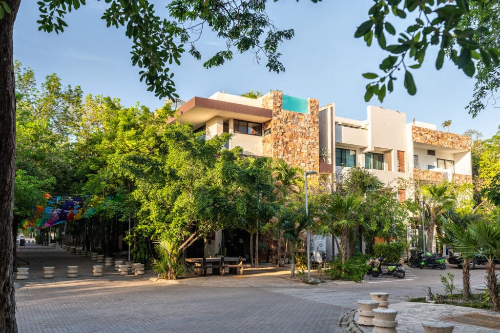 Modern multi-unit condo and commercial building in Aldea Zama, Tulum, surrounded by lush greenery and palm trees.