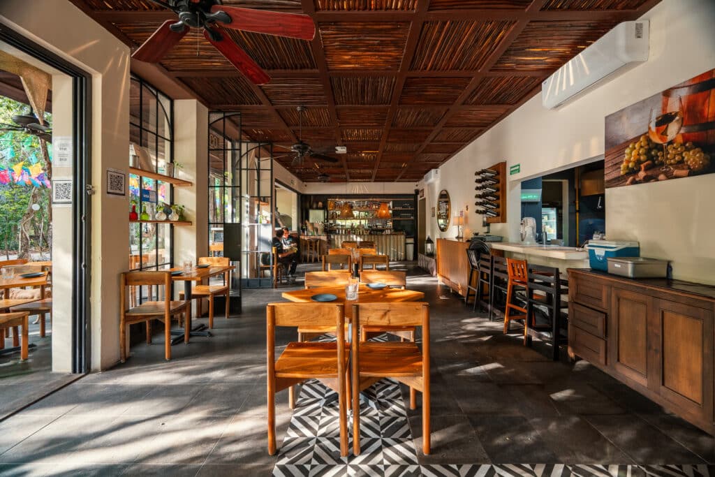 Interior view of 3 Condos And Comercial Space Building in Aldea Zama, Tulum, showing a cozy dining area with wooden tables, chairs, and a bar in the background.
