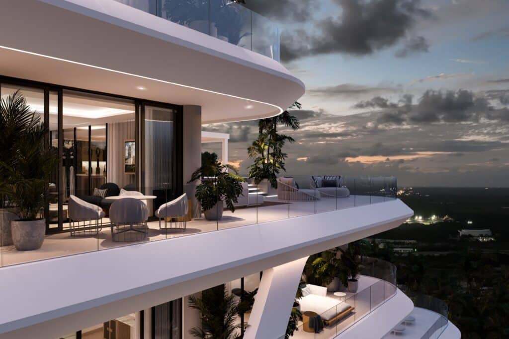 Modern apartment balcony at Nautica 402 in Cancun's Laguna Nichupte, featuring sleek furniture, potted plants, and glass railings with a city and sunset view.