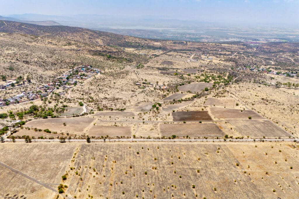 Aerial view of land in Rancho Guadalupe development in San Miguel de Allende's Alcocer area, showing plots, sparse vegetation, and distant hills under a clear sky.