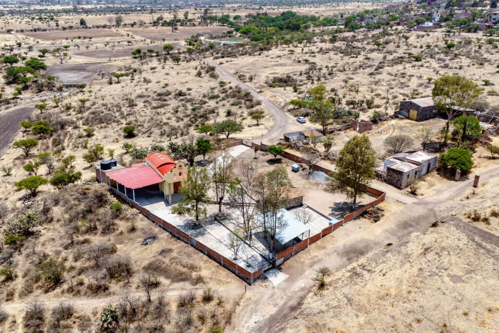 Aerial view of Rancho Guadalupe in San Miguel de Allende, showing a property with a red-roofed building, a white canopy, and surrounding trees and fencing in a dry, semi-arid landscape.