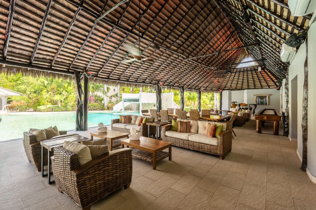 A spacious outdoor lounge area at Rancho Paraiso Oasis in Akumal features wicker furniture, colorful cushions, and a view of the pool surrounded by lush jungle greenery.