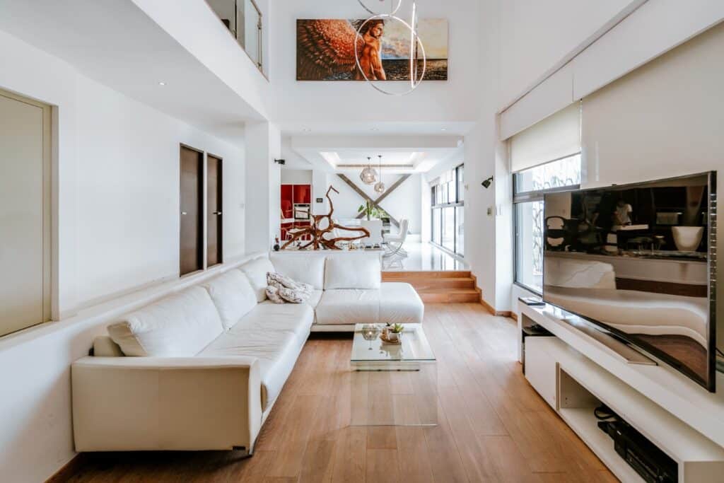 Living room in Torre Onze Penthouse 3, Merida, featuring white leather sectional sofa, wooden flooring, large flat-screen TV, and modern decor with natural light.