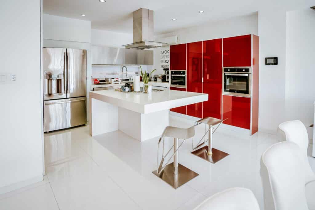 Modern kitchen in Torre Onze Penthouse 3, Merida, featuring white countertops, red cabinetry, stainless steel appliances, and a central island with seating.