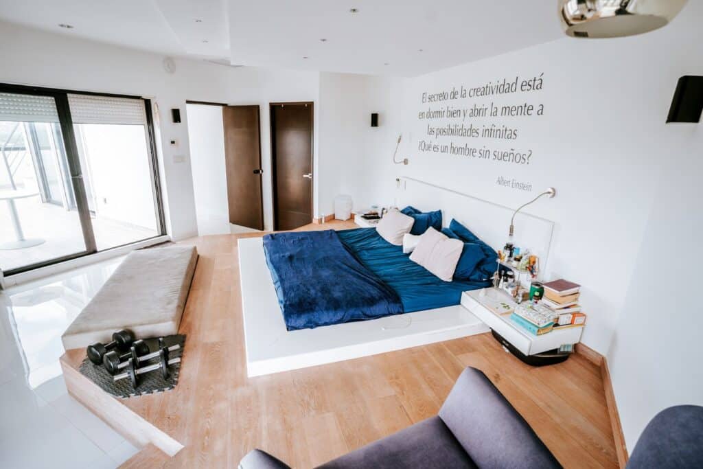 Interior bedroom of Torre Onze Penthouse 3 in San Gertrudis Copo, Merida, featuring a bed with blue bedding, a bench, dumbbells, and a wall quote by Albert Einstein.