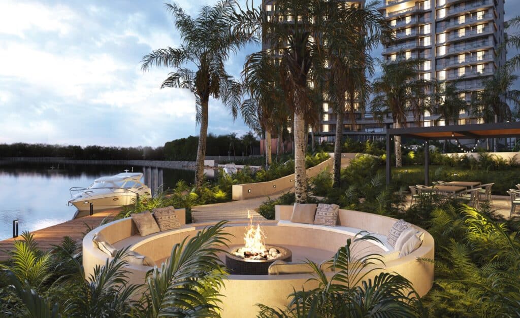 A scenic evening view at Velmari 604 in Puerto Cancun, featuring a waterfront area with yachts, lush greenery, and a cozy fire pit surrounded by seating.