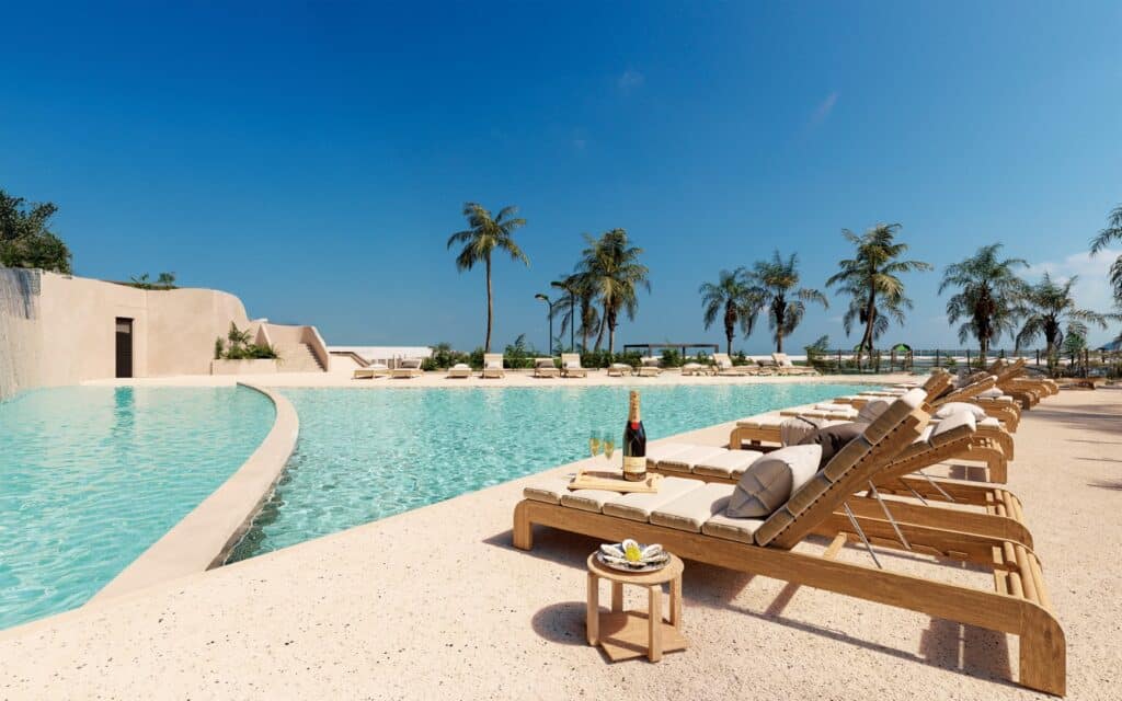A scene from Velmari 604 in Puerto Cancun, showing an outdoor swimming pool with sun loungers, a small table with champagne, and tall palm trees under a clear blue sky.