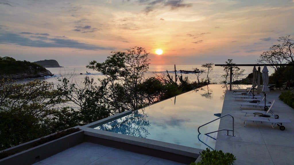 An ocean view from the Amanecer J2 development in Playa Arrocito, Huatulco, featuring a terrace with a pool overlooking the sunset over the sea and surrounding coastline.