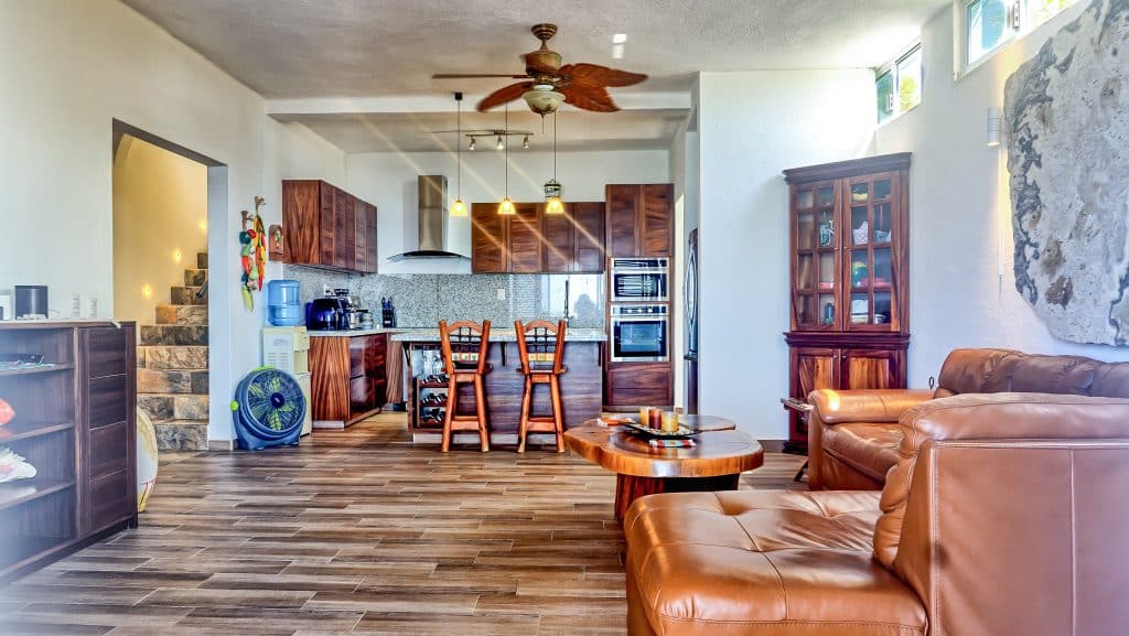 Interior view of Casa Salchi in Huatulco, showing a living area with leather sofas, wooden cabinets, and an open kitchen with