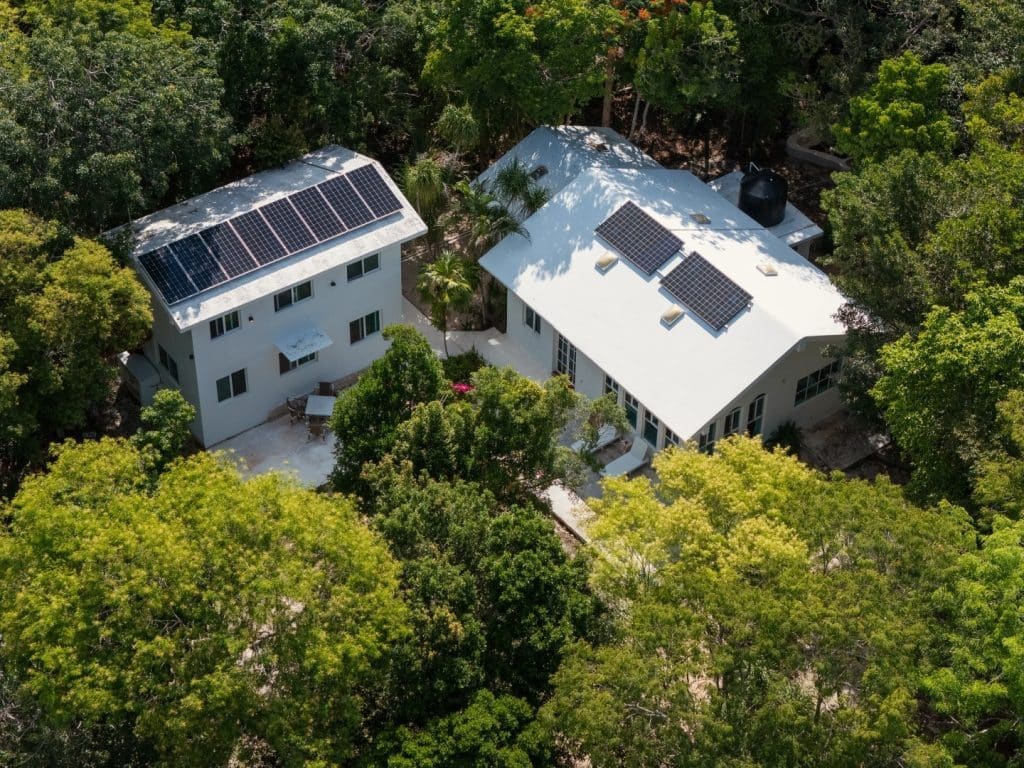 An aerial view of Jungle Homes on 2.5 Acres in Puerto Aventuras, Xpu Ha, showing two white houses surrounded by dense green trees, each equipped with solar panels on the roofs.