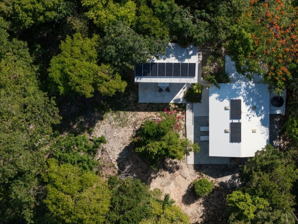 Aerial view of Jungle Homes on 2.5 Acres in Puerto Aventuras, showing two white buildings with solar panels surrounded by lush greenery and trees in Xpu Ha.