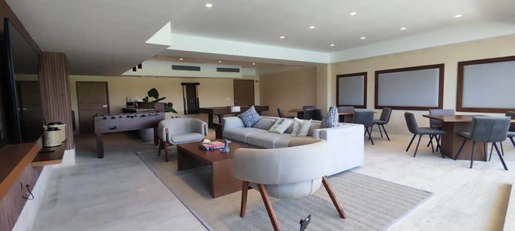 Interior view of a spacious, modern living area in La Vela 412 development, Cancun, featuring a comfortable sofa, stylish chairs, and a game table with neutral tones and contemporary decor.