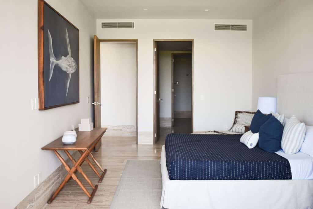 Furnished bedroom in La Vela 412, Puerto Cancun, featuring a bed with navy and striped pillows, a wooden side table, and a painting on the wall.