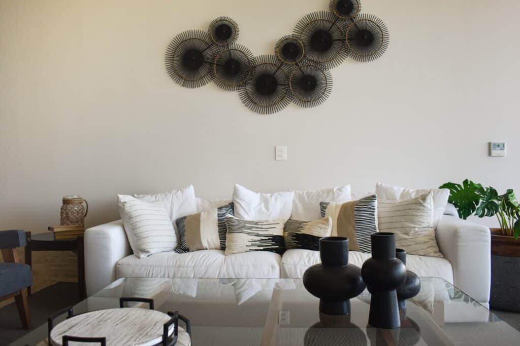 A spacious living room in La Vela 412, Cancun, featuring a white sofa with patterned pillows, a glass coffee table with black decorative vases, and wall art above.