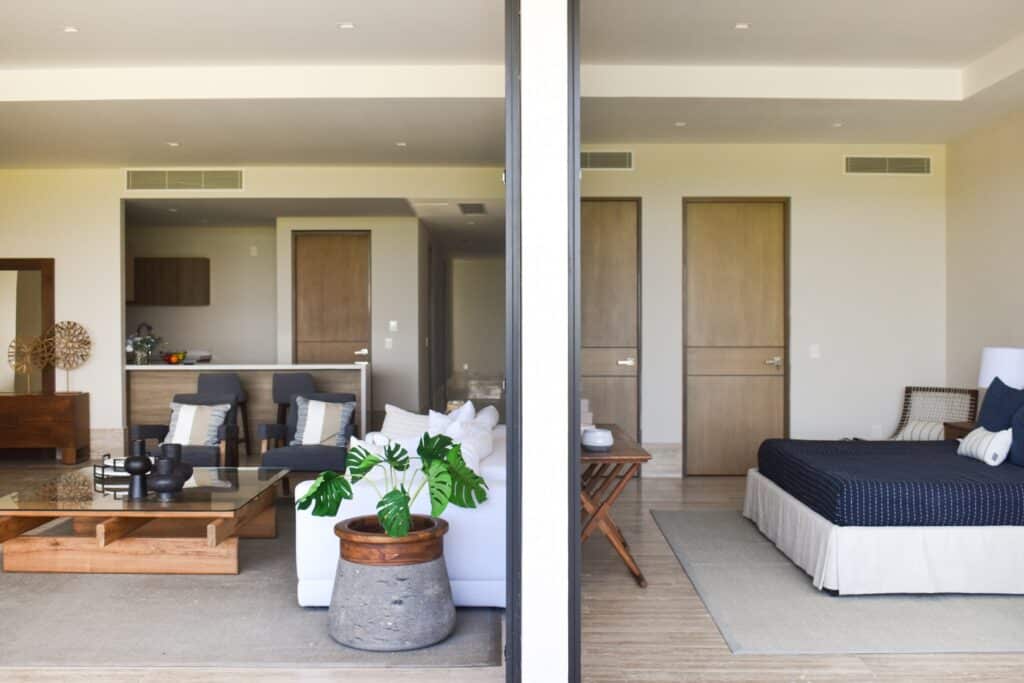 Interior view of La Vela 412 in Puerto Cancun, featuring a living area with a sofa, chairs, and decor, and a bedroom with a bed and nearby furniture.