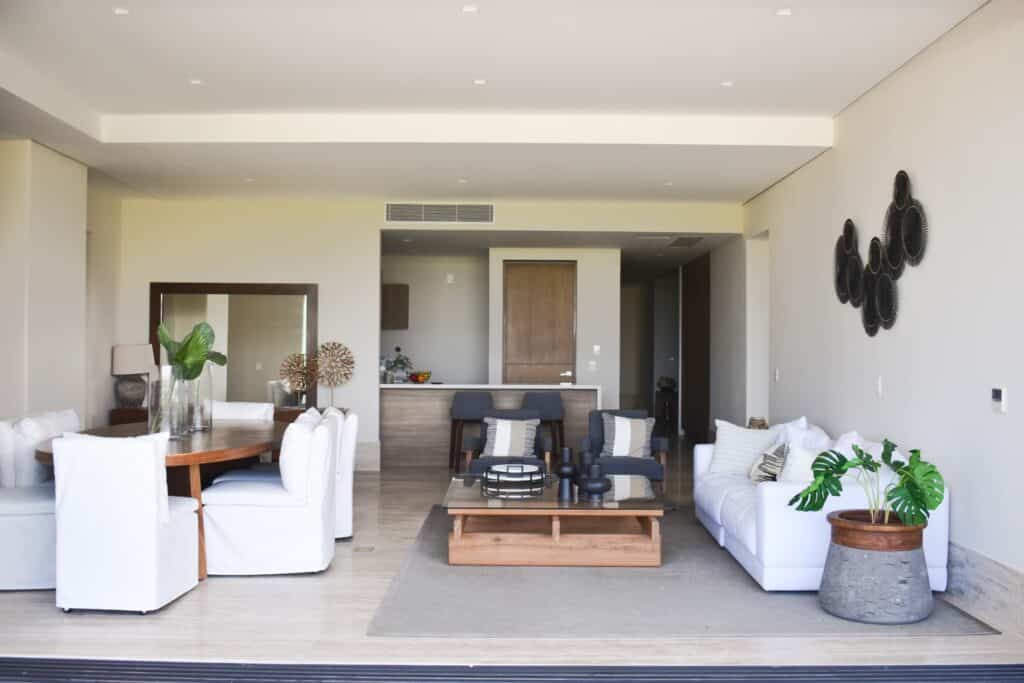 Living room inside La Vela 412 development in Puerto Cancun, featuring white and gray furniture, decorative plants, and modern wall art.