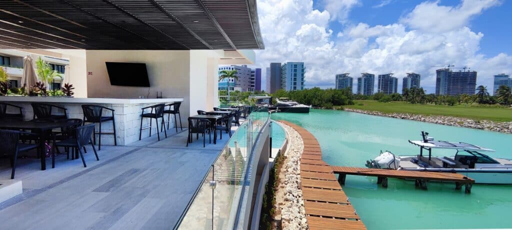 A spacious balcony at La Vela 412 in Puerto Cancun, overlooking a canal with boats, surrounded by modern high-rise buildings and a blue sky with clouds.