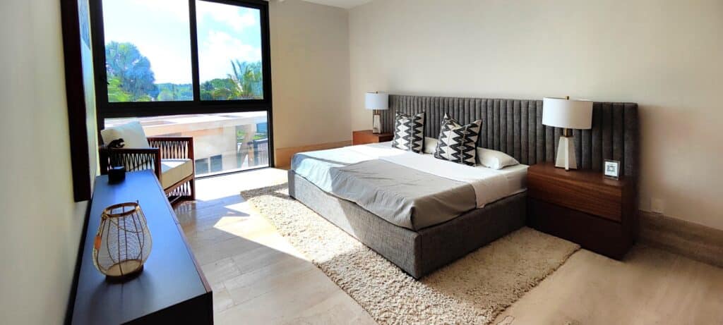 A bedroom in La Vela 412, located in Cancun's Puerto Cancun area, features a large bed with a textured headboard, two side tables with lamps, a dresser, and a floor-to-ceiling.