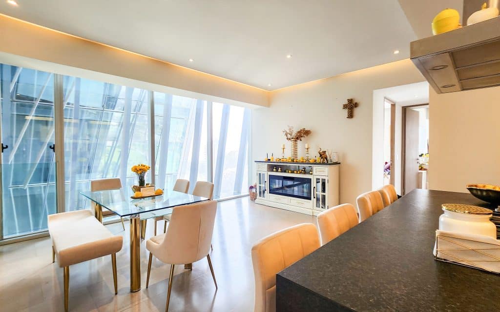 Modern dining and living area in Paradox 24 A, Santa Fe, Mexico City, featuring a glass-top dining table, beige chairs, and a white cabinet with decorative items.