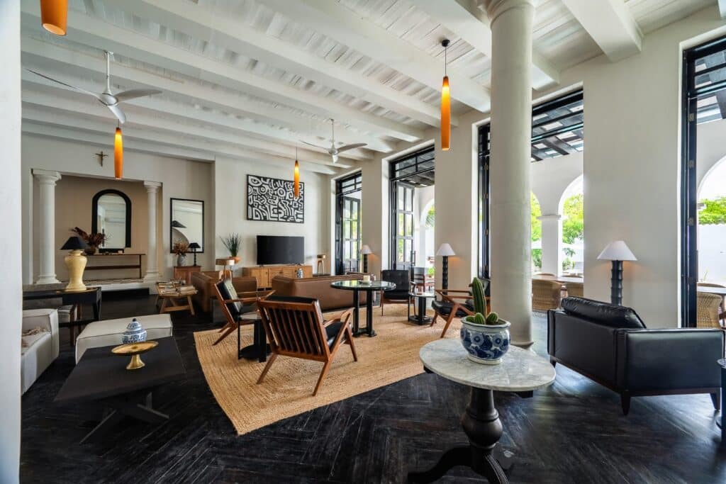 Interior of Rae’s Villa in Tulum with white walls, dark flooring, wooden furniture, and large windows overlooking greenery