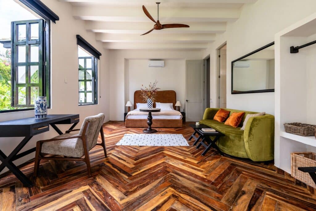 Living room in Rae’s Villa, Tulum with white walls, wooden floors, green sofa, bed, and large windows
