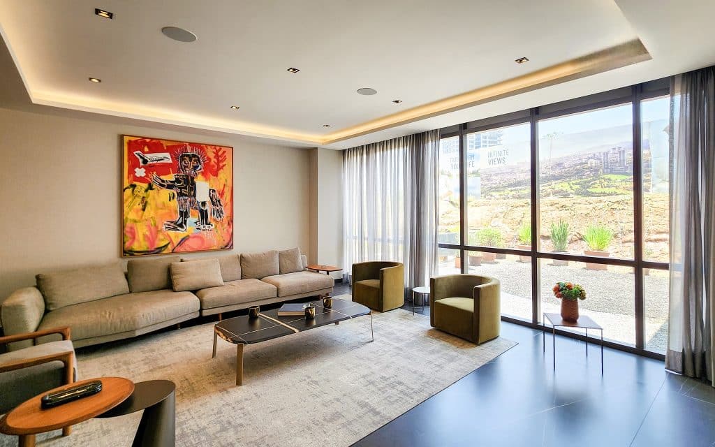 Living room in Sky View Condo, Mexico City, featuring a beige sofa, green armchairs, abstract wall art, and large windows with city and landscape views.