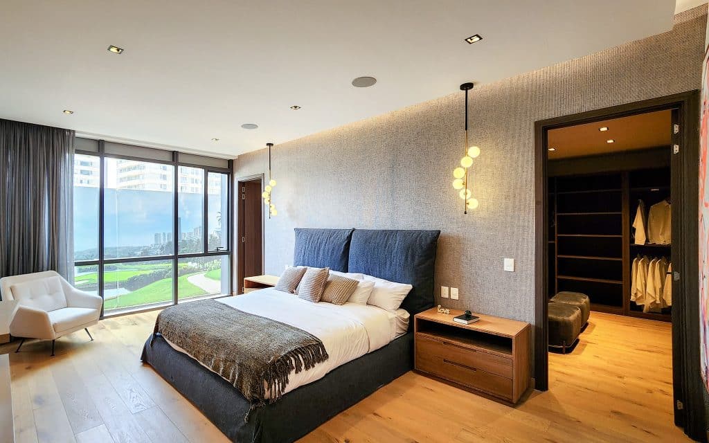 A bedroom in Sky View Condo, Naucalpan de Juarez, Mexico City, featuring a large bed with a dark upholstered headboard, wooden nightstands, a white armchair, and a view of the.