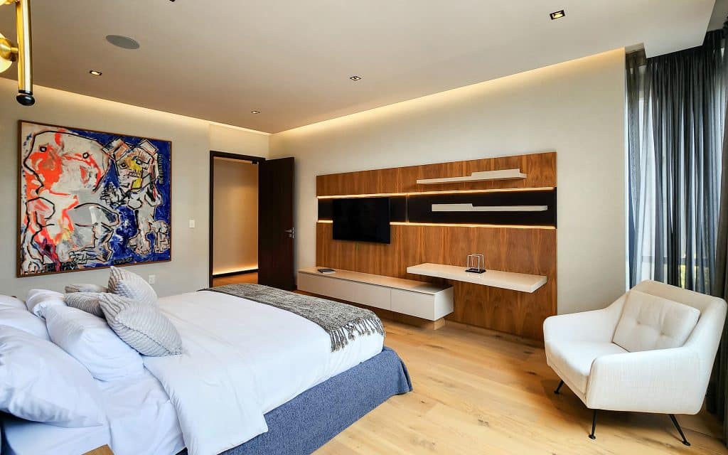 A modern bedroom at Sky View Condo in Naucalpan De Juarez, Mexico City, featuring a large bed, a white armchair, a colorful abstract artwork, and a sleek wall-mounted TV.
