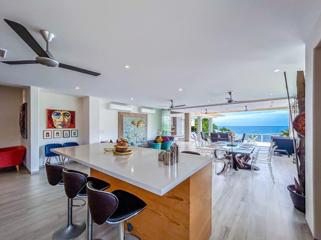Interior view of Villa Montecarlo in Playa Arrocito, Huatulco, featuring an open-concept living and dining area with modern furniture, artwork, and an ocean view through large windows.