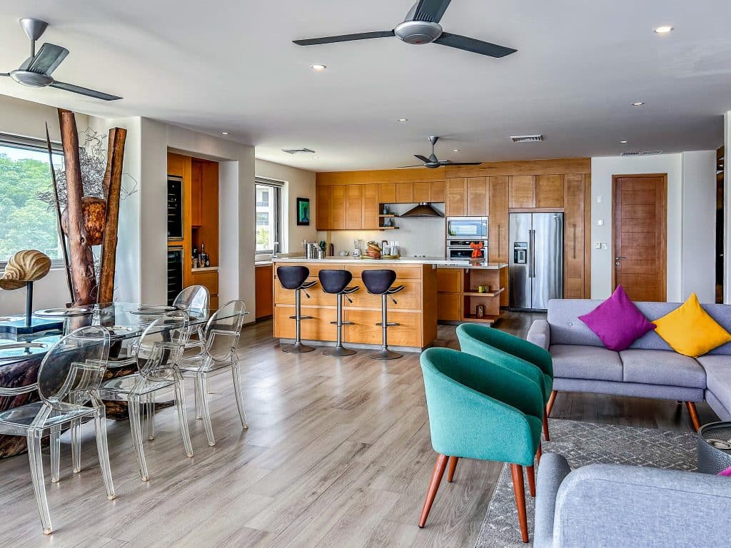 Interior view of Villa Montecarlo in Playa Arrocito, Huatulco, showcasing an open-concept living area with a modern kitchen, colorful seating, and natural light.