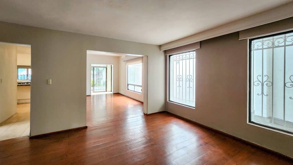 A spacious living area with wooden flooring and large windows at Milton 64 in Mexico City’s Miguel Hidalgo, providing abundant natural light and views.