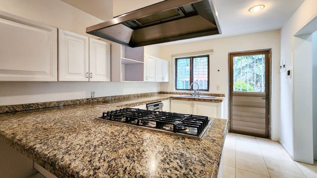 A kitchen with granite countertops and white cabinetry at Milton 64 in Mexico City, featuring a window, a door with a metal screen, and a range hood above the stove.