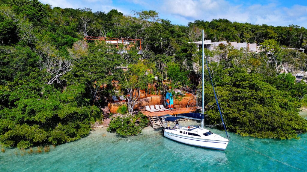 Lake front view of 13-room Bacalar hotel with boat docked on turquoise waters surrounded by lush greenery