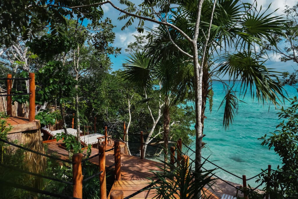 Wooden deck with lounge chairs amid lush trees overlooking turquoise Lake Bacalar in Bacalar development