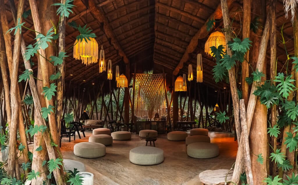 Interior view of the 13-Room Lake Front Bacalar Hotel with wooden beams, hanging lanterns, and lush green plants