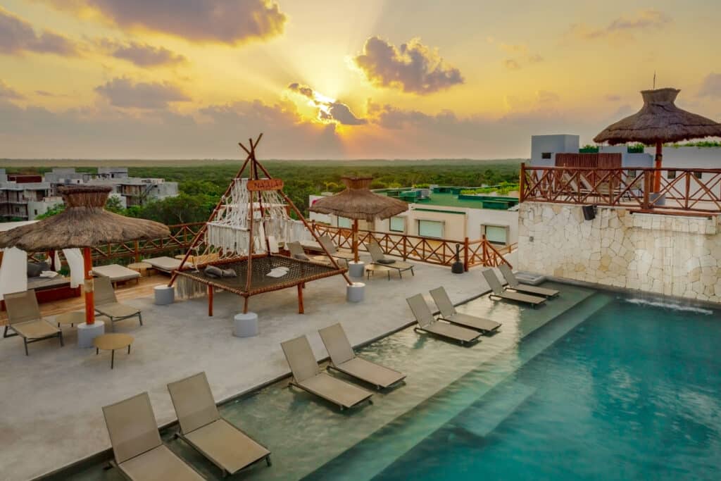 Sunset over the pool area at Tulum 95 Room Hotel in Tulum Centro, featuring straw umbrellas, lounge chairs, and a scenic view