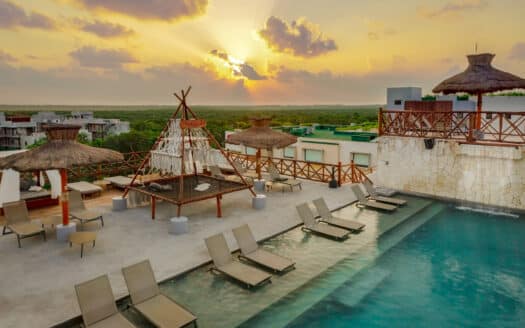 Sunset over the pool area at Tulum 95 Room Hotel in Tulum Centro, featuring straw umbrellas, lounge chairs, and a scenic view