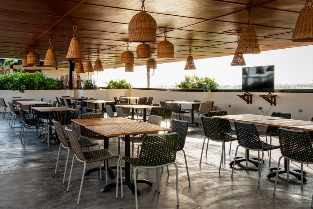 Indoor dining area at Tulum 95 Room Hotel in Tulum, with wooden ceiling, wicker pendant lights, tables, and chairs