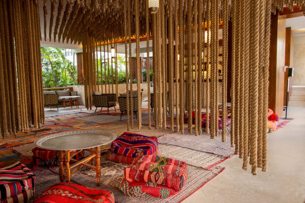 Interior of Tulum 95 Room Hotel in Tulum, featuring woven ropes, colorful cushions, and seating area with lush greenery