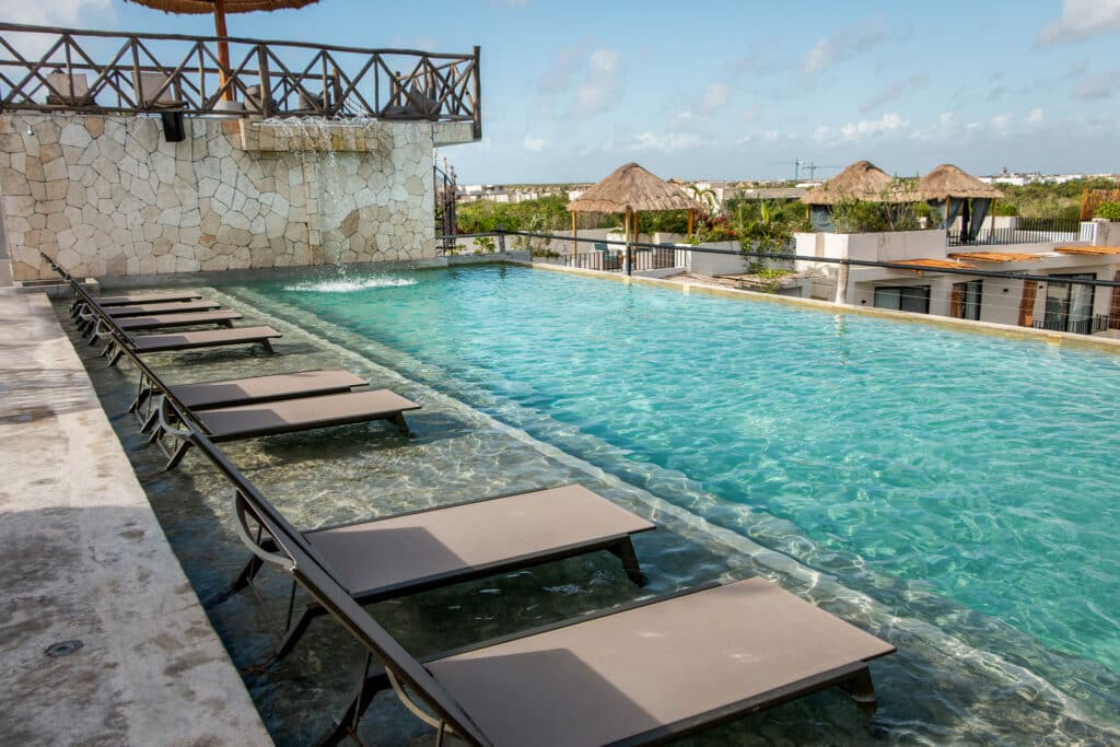Swimming pool with lounge chairs at Tulum 95 Room Hotel in Tulum Centro, featuring a stone wall and views of thatched roof