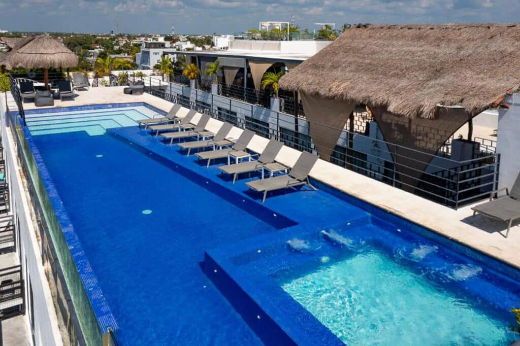 An aerial view of the rooftop swimming pool at 82 Room Playa del Carmen Hotel in Playa del Carmen, featuring sun loungers, shaded sitting areas, and surrounding cityscape.