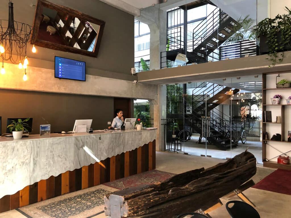 The lobby of the 82 Room Playa del Carmen Hotel in Playa del Carmen features a modern industrial design with a marble reception desk, decorative lighting, and an open staircase leading to the upper level.