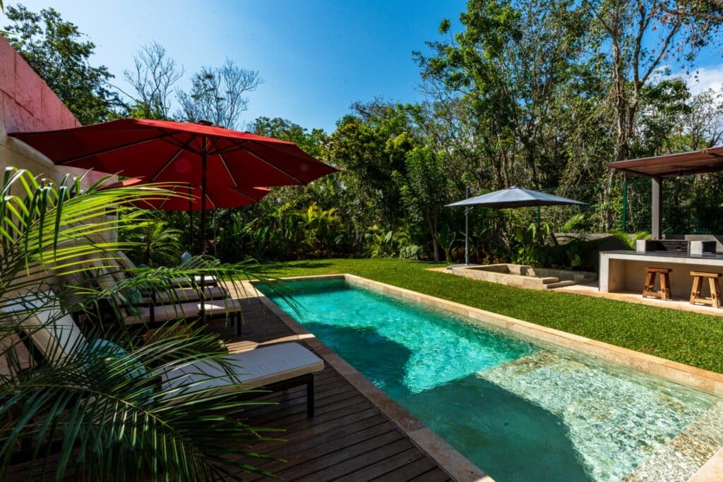 A house with a swimming pool surrounded by lush greenery and shaded lounge chairs at Brisas 45 villa in Xpu Ha, Playa del Carmen.