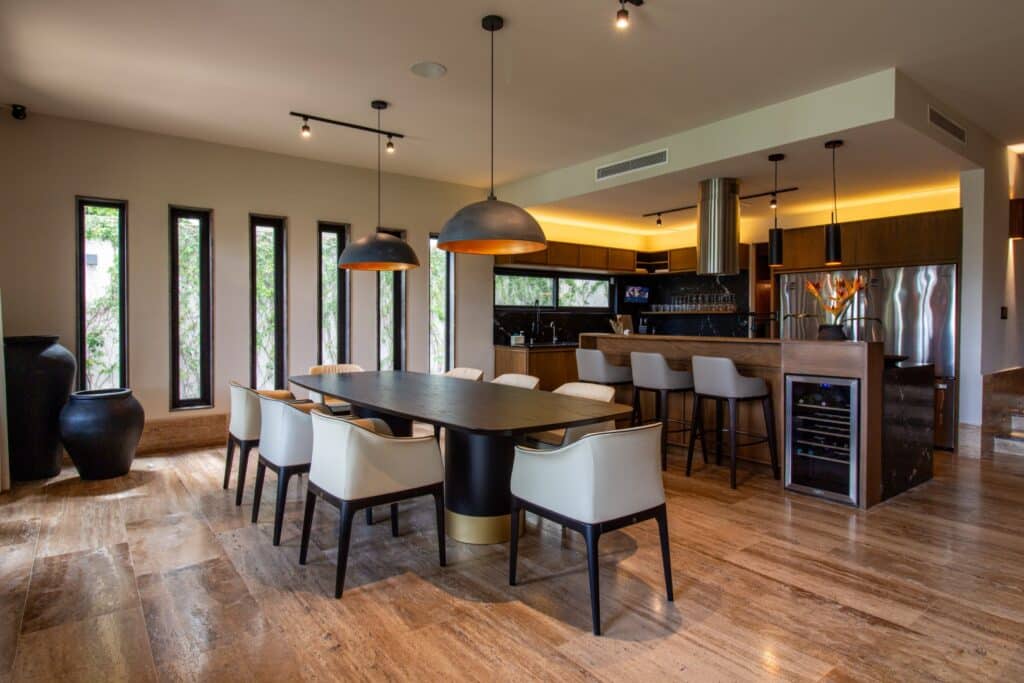 Interior view of Villa Flamingos in Cancun's Marina Front area, featuring a dining area with a large wooden table, white chairs, and a modern open kitchen with bar seating.