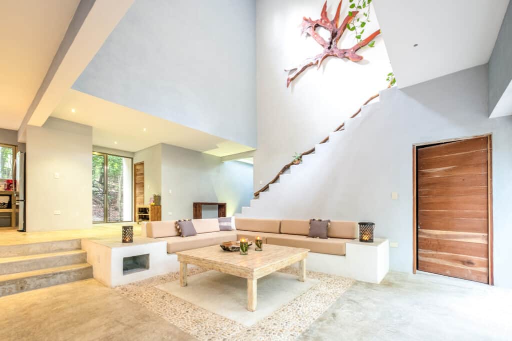 Interior living area of Bacalar luxury lakefront estate villa, featuring a beige sectional sofa, rustic wooden coffee table, and a high ceiling with natural light.